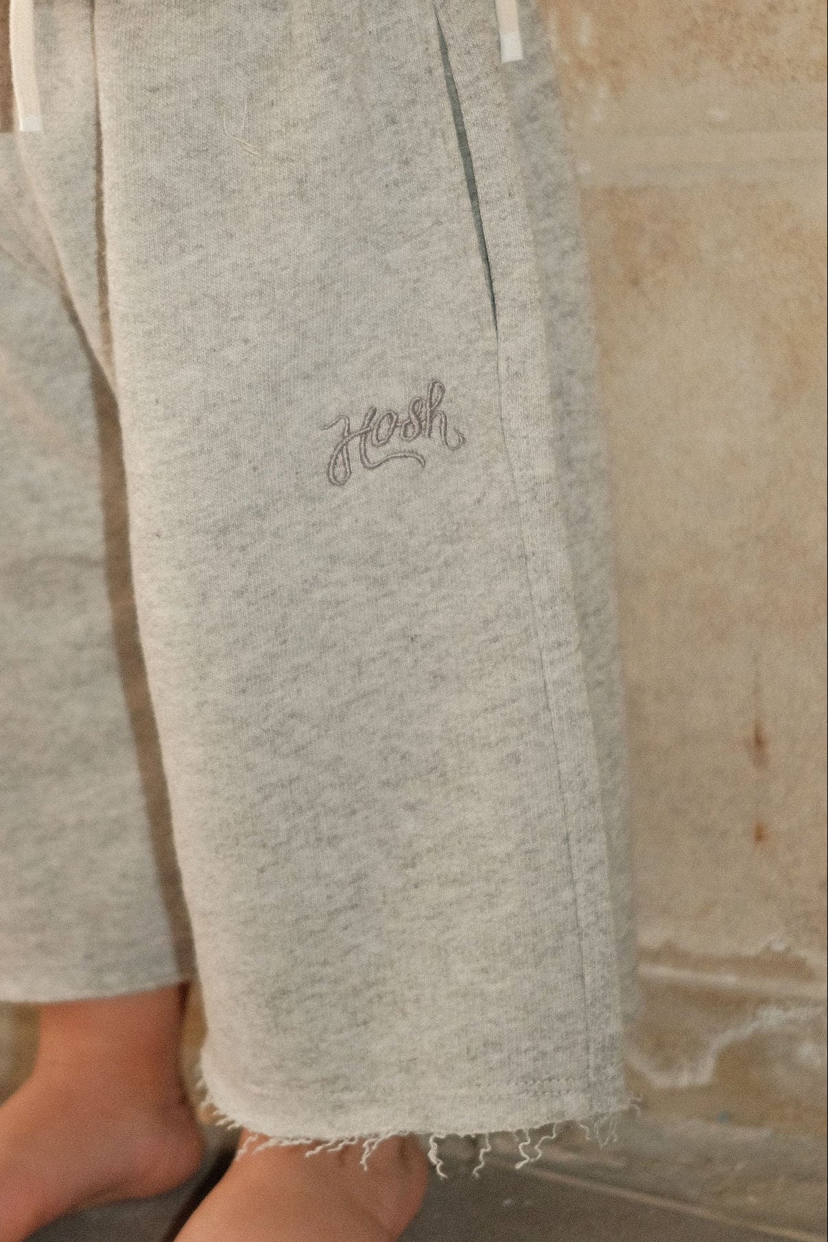 Child wearing gray pants and a white top with red sleeves against a stone wall.