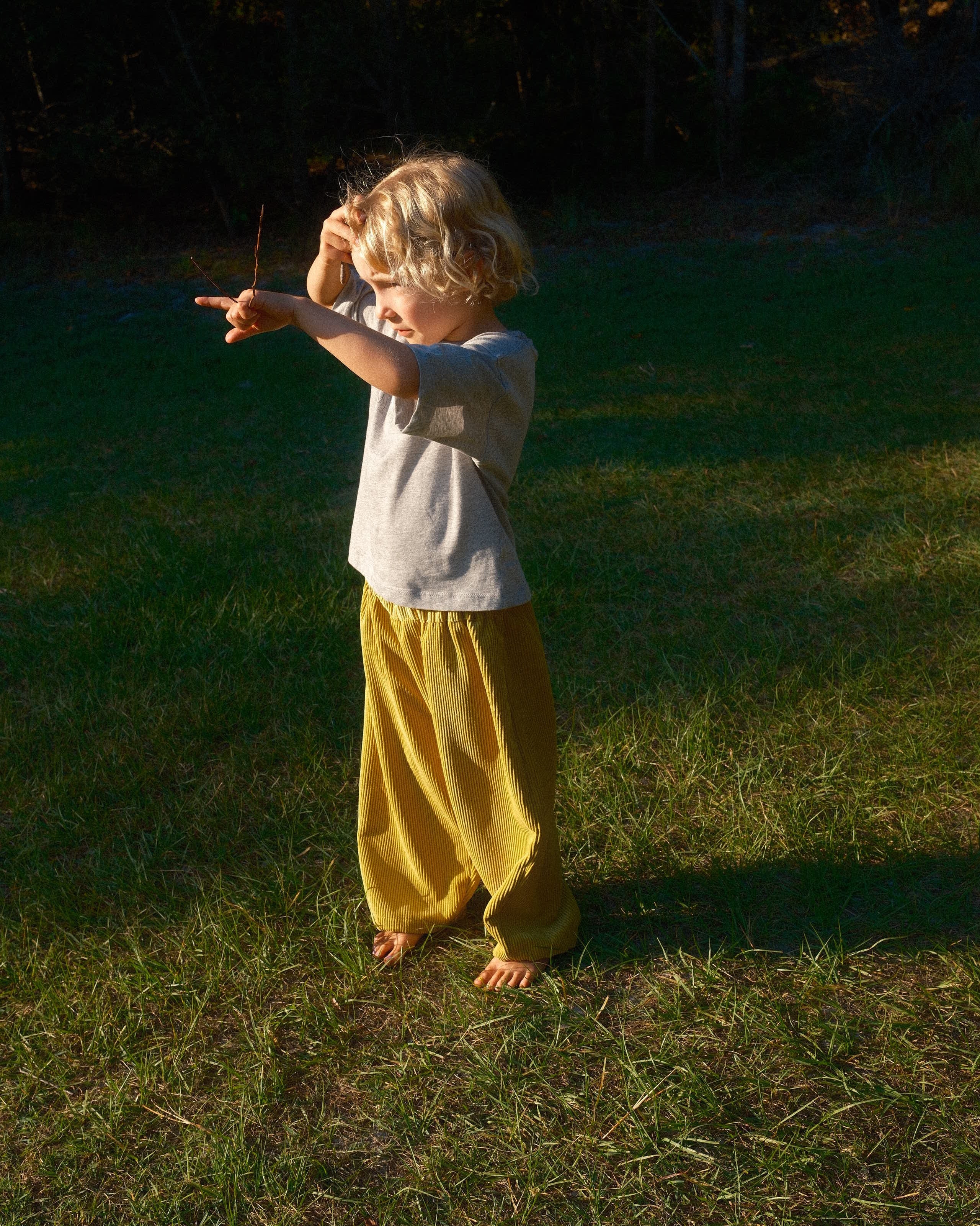 Child in a yellow dress standing on grass with a long shadow