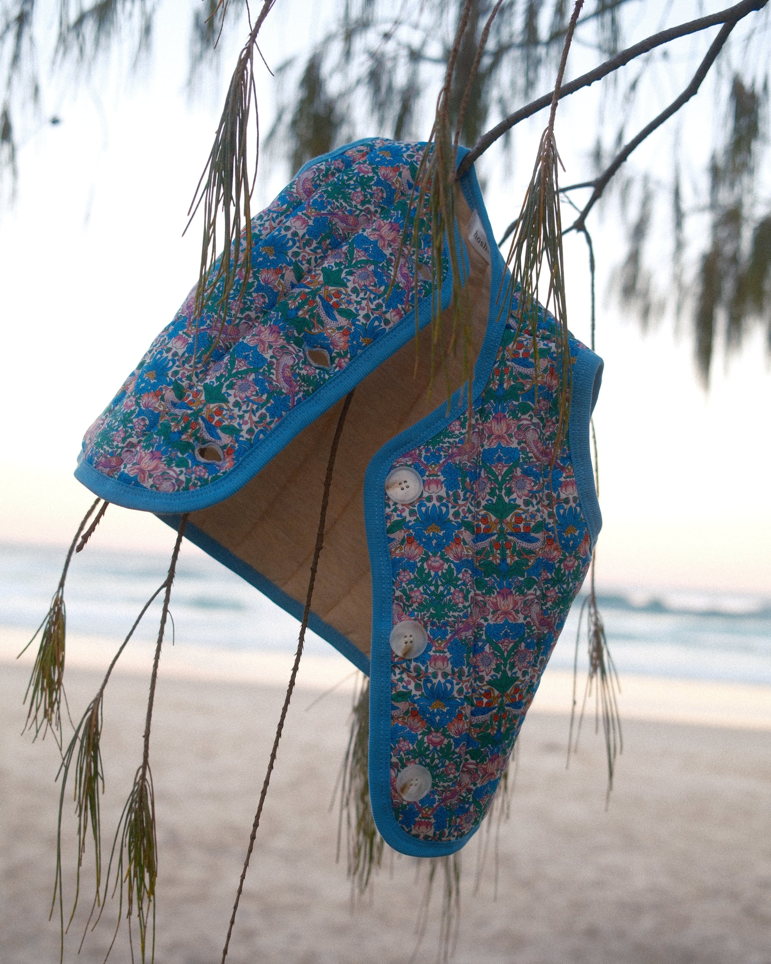 Pair of blue floral-patterned shoes on a reflective surface with trees in the background