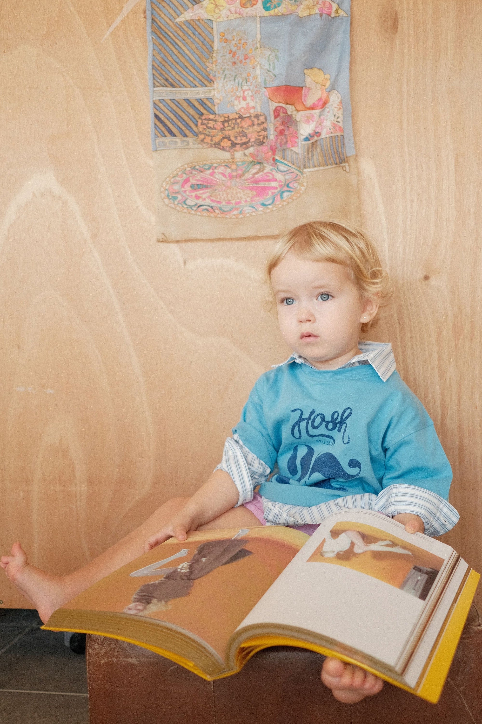 Child sitting on a box holding a book with a wooden wall and poster in the background