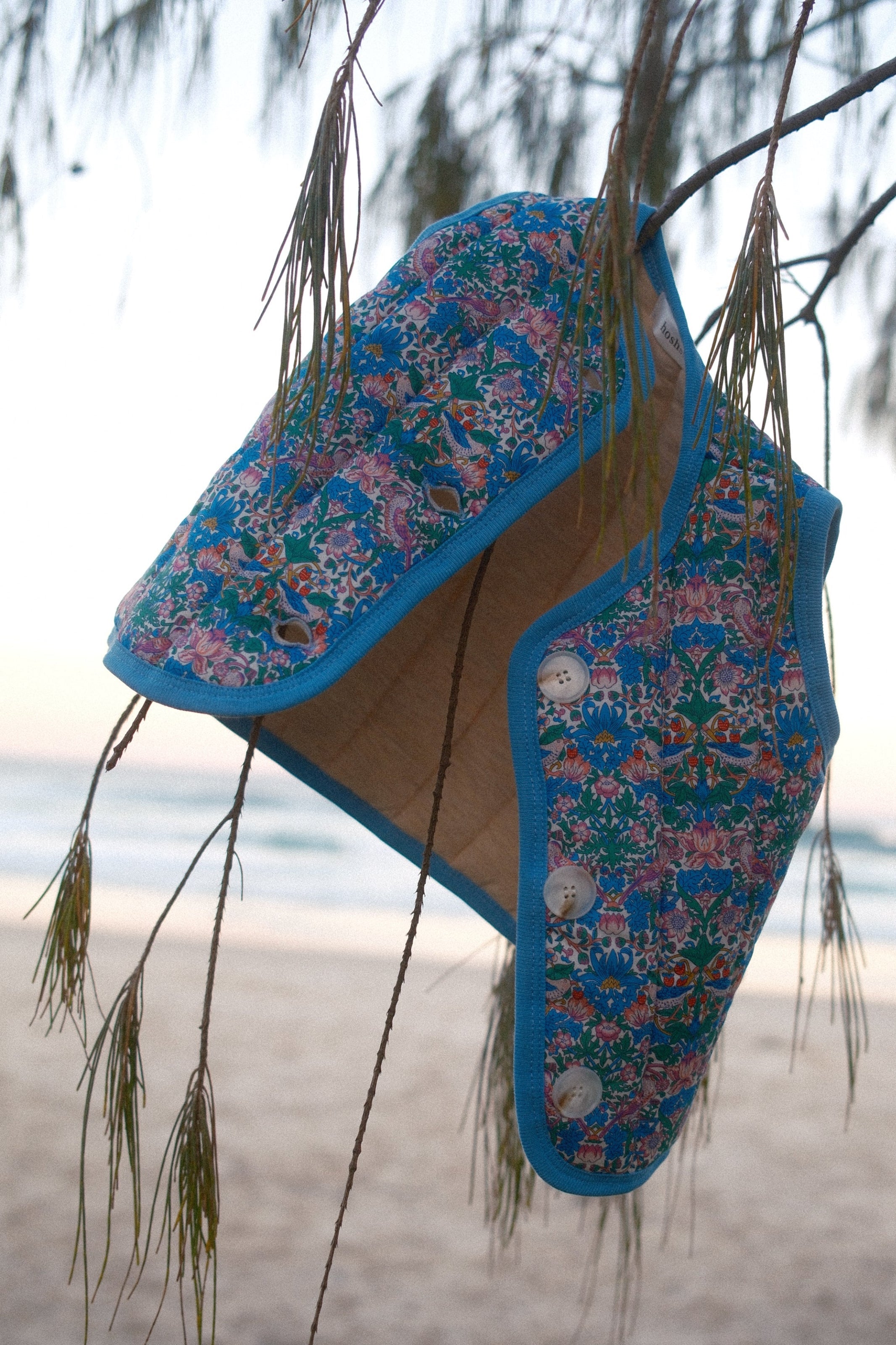 Pair of blue floral-patterned shoes on a reflective surface with trees in the background